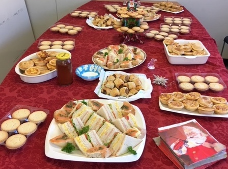 Table with festive red table cloth and Christmas-theme serviettes, covered with plates of hot savouries, sandwiches, tarts and other snacks 